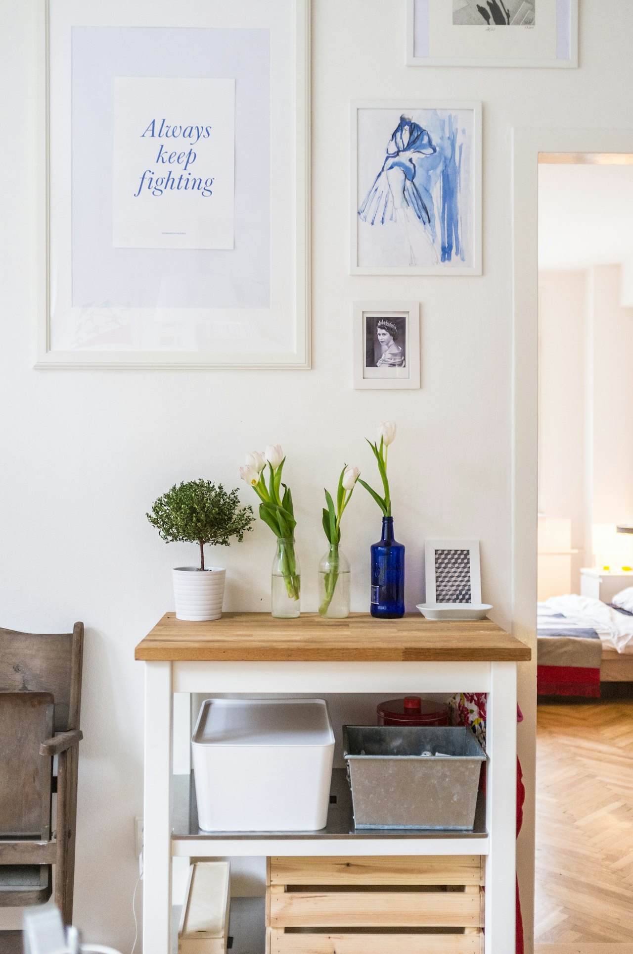 Minimalist home decor with a wooden console table featuring potted plants, white tulips in glass vases, and framed artwork on a white wall